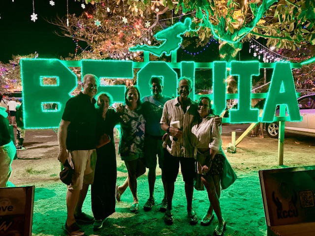 Friends posing in front of a bright Bequia sign at night